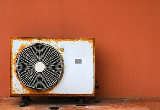 Old heat pump outdoor unit outside up against wall